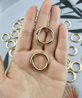 Hand holding two gold 1 inch metal spring O rings with round carabiner clips from 50 Pack 1 Inch Metal Spring O Rings Set With Round Carabiner Clips Snap Hooks For Keychains Purses Shoulder Bags And DIY Crafts In Gold Finish Durable And Handy For Busy DIYers On The Go.