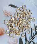 50 Pack 1 Inch Metal Spring O Rings Set With Round Carabiner Clips Snap Hooks For Keychains Purses Shoulder Bags And DIY Crafts In Gold Finish displayed on plate with seashells.