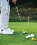 Person practicing putting on a golf course with Practice Golf Balls - 24 Pack Colored Plastic Balls 41mm Training Realistic Feel Limited Flight