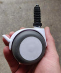 Hand holding a plastic caster with a stem grip, showing a single wheel from the 20 Pcs Plastic Round Caster Wheel Socket Sleeve Caps set.