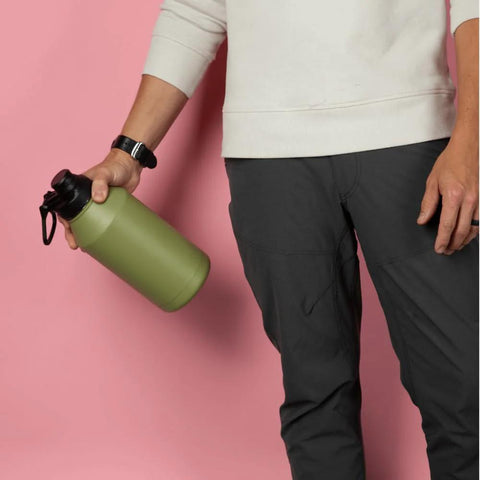 Person holding a green water bottle against a pink background, wearing a white sweatshirt and dark pants.