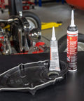 Two tubes of RTV Grey High Performance Silicone Gasket Maker For Oil Resistant Seals in a garage with auto parts