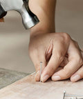 Person hammering a silver nail from 600 Piece Nail Assortment Kit Silver Nails In 4 Sizes For Hanging Pictures And Finishing Nails.