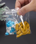 Person holding 300 PCS Small Plastic Bags Set In 3 Sizes 2x2.5in, 2.2x3in, 3x3.5in Resealable Clear Poly Bags with colorful pills