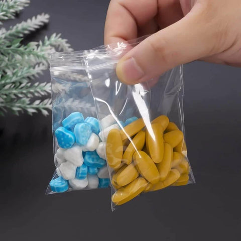 Person holding 300 PCS Small Plastic Bags Set In 3 Sizes 2x2.5in, 2.2x3in, 3x3.5in Resealable Clear Poly Bags with colorful pills