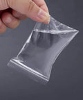 Hand holding a clear small plastic bag from 300 PCS Small Plastic Bags Set In 3 Sizes 2x2.5in, 2.2x3in, 3x3.5in Resealable Clear Poly Bags.