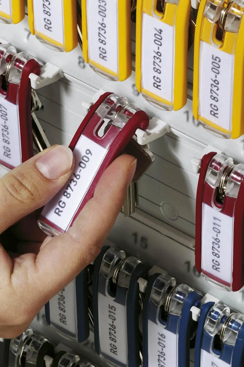 Hand pulling a red key tag from a wall-mounted key cabinet holding 36 key tags, in a heavy-duty brushed aluminum box with combination lock.