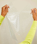 Hands tearing clear perforated bubble cushioning wrap for fragile items perforated 12 inch roll 175 ft clear with small three sixteenth inch bubbles.