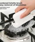 Hand using a hardened bristle brush to clean a stovetop burner, demonstrating effective removal of grime with a removable brush and scraper.