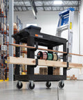 Front view of Heavy Duty Plastic Utility Cart For Warehouses And Workshops With Three Shelves 32 By 18 Rolling Tub Cart 300 Lb Capacity Ergonomic Push Handle Black By Luxor in a warehouse setting.