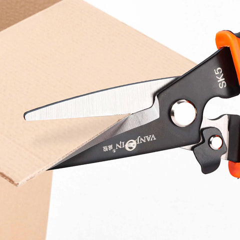 Heavy Duty 9 Inch Multipurpose Scissors With Serrated Edge cutting cardboard, featuring spring loaded steel shears for industry and home use.
