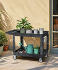 Heavy Duty 2 Shelf Plastic Utility Service Cart On Wheels With 550 Lb Capacity And 45 X 25 Inch Size Rugged Rolling Work Cart For Warehouse Garage School And Office Corrosion Resistant And Built Tough Black, holding plants and garden tools.
