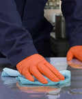 Person wearing Hi Vis Orange Nitrile Gloves Raised Diamond Texture 8 Mil using cloth to clean surface, showcasing grip and durability