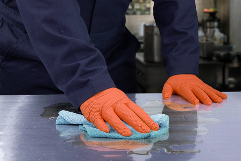 Person wearing Hi Vis Orange Nitrile Gloves Raised Diamond Texture 8 Mil using cloth to clean surface, showcasing grip and durability