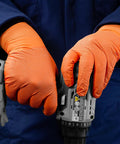 Person wearing Hi Vis Orange Nitrile Gloves Raised Diamond Texture 8 Mil using a power tool in workshop