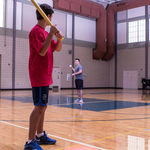 Indoor practice with 9" Hollow Plastic Baseballs - Athletic Baseball Equipment in gym, player ready to bat with a lightweight plastic bat.