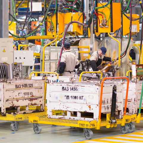 Industrial workshop with workers operating machinery and using heavy duty platform trucks with 5 by 2 inch casters.