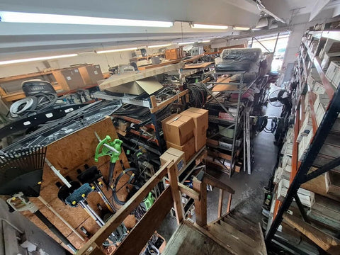 Storage room with shelves filled with various industrial and marine equipment, boxes, cables, and hardware parts.