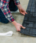 Person installing carpet tile with Heavy Duty Double Sided Tape For Carpet Tiles And Vinyl Flooring, Ideal For Artificial Grass, Foam Gym Tiles And Rubber Interlocking Gym Tiles, Easy Installation With Ultra Strong Grip And Industrial Strength Bond No Mess