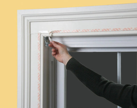 Person applying Indoor Window Shrink Kit For 42 To 62 Inch Windows Clear 9 Pack Insulation Film to window frame
