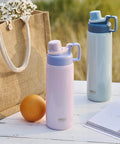 Two pastel insulated stainless steel water bottles with spout lids on a picnic table, one light pink and one light blue.
