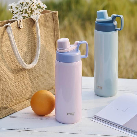 Two pastel insulated stainless steel water bottles with spout lids on a picnic table, one light pink and one light blue.
