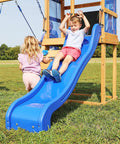 Children playing on a blue slide attached to a wooden play structure in a grassy field.