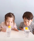 Two children playing a game with 40mm colorful table tennis balls on glass cups, using 185 Pcs Colorful Table Tennis Balls for kids' fun activities.