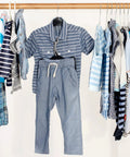 Children's striped shirt and gray pants on a wooden clothing rack with various kids' outfits in blue and white tones.