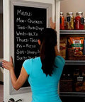 Person adjusting a blackboard menu on a pantry door, showing weekly meal plan and stocked shelves with food items.