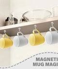 Yellow and white mugs hanging from magnetic hooks under a kitchen shelf with bowls and glasses displayed above.