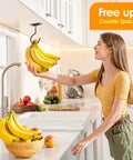 Woman in kitchen reaching for bananas hanging from under-cabinet hook with counter space saver sign