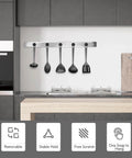 Modern kitchen with wall-mounted utensil holder, four black cooking utensils hanging above a counter, focus on minimalist design and functionality.