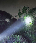 Solar Rechargeable Multi Function 1000 Lumens LED Flashlight With Emergency Strobe Light illuminating a tree at night outdoors