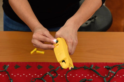 Person using The Complete LED Christmas Holiday Light Set Repair Tool to fix string lights on a table.