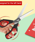 Heavy Duty All Purpose Fabric Scissors For Sewing And Garment Making With Stainless Steel Blades held in left hand next to craft paper
