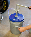 Person using OTC 2352 Lever Action Bucket Pump on 5-gallon pail with handle and hose visible in a garage setting.