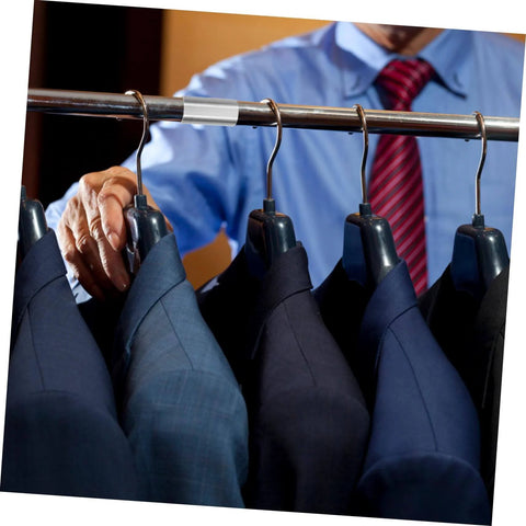 Man selecting a suit from a rack with various dark-colored suits and ties in a clothing store setting.
