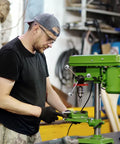 Worker using green industrial drill press in workshop.