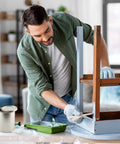 Man painting a chair with Empty Quart Paint Cans With Lids Pack Of 2 Unlined Metal Cans For Solvents in a living room setting.
