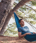 Man relaxing in a blue hammock tied to trees in a forest setting