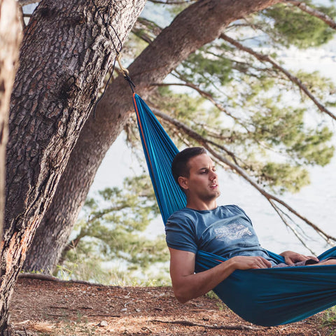 Man relaxing in a blue hammock tied to trees in a forest setting