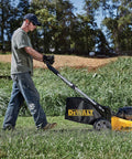 Man using yellow and black Dewalt lawnmower in grassy field.