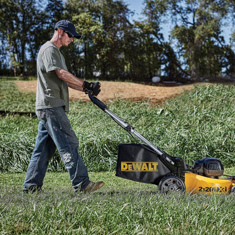 Man using yellow and black Dewalt lawnmower in grassy field.