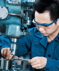 Worker operating a machine in a workshop, wearing protective goggles and blue uniform, focusing on precision measurement.