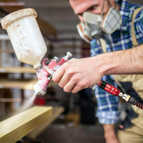 Person using spray gun with red Five In One Universal Quick Connect Air Coupler for 1/4 inch female NPT industrial hose fittings.