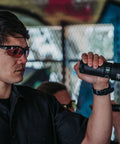 Man wearing Harrier Interchangeable Shooting Glasses with tinted lenses holding a flashlight in urban environment.