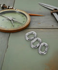 Three 8mm stainless steel marine-grade quick link connectors on a wooden surface