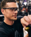 Man wearing Matte Black Frames Shooting Glasses With ANSI Z87 Safety And Changeable Lenses, focused on task in workshop.