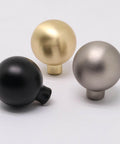 Three assorted cabinet knobs, including matte black, brass, and matte gray zinc alloy, each with a round ball design, ideal for drawers.